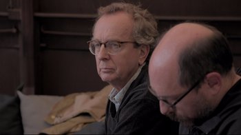 Movie still from “Billie Eilish: The World's a Little Blurry” (2021), directed by R.J. Cutler – A man with glasses is sitting next to another man; Close Up shot, Over the shoulder angle