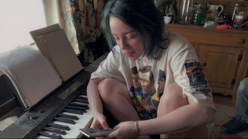 Movie still from “Billie Eilish: The World's a Little Blurry” (2021), directed by R.J. Cutler – A woman sitting on the floor looking at her phone; Medium shot, High angle