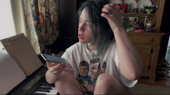 Movie still from “Billie Eilish: The World's a Little Blurry” (2021), directed by R.J. Cutler – A woman sitting on the floor holding a cell phone; Medium shot, High angle