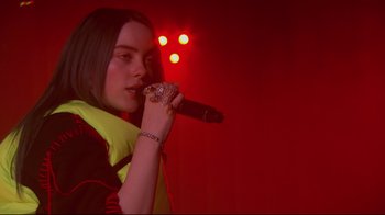 Movie still from “Billie Eilish: The World's a Little Blurry” (2021), directed by R.J. Cutler – A woman holding a microphone up to her mouth; Close Up shot, Over the shoulder angle
