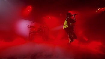 Movie still from “Billie Eilish: The World's a Little Blurry” (2021), directed by R.J. Cutler – A person standing on a stage with a microphone; Wide shot, Low angle
