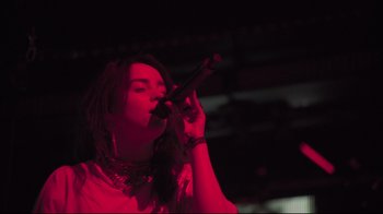 Movie still from “Billie Eilish: The World's a Little Blurry” (2021), directed by R.J. Cutler – A woman with dreadlocks is singing into a microphone; Close Up shot, Low angle