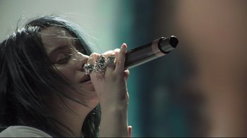 Movie still from “Billie Eilish: The World's a Little Blurry” (2021), directed by R.J. Cutler – A woman holding a microphone up to her mouth; Close Up shot, Low angle
