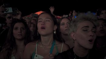 Movie still from “Billie Eilish: The World's a Little Blurry” (2021), directed by R.J. Cutler – A group of people that are sitting in a crowd; Medium shot, Low angle