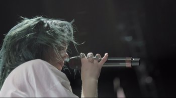 Movie still from “Billie Eilish: The World's a Little Blurry” (2021), directed by R.J. Cutler – A woman with green hair is holding a microphone; Extreme Close Up shot, High angle