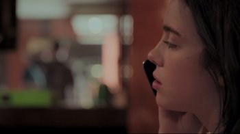 Movie still from “Billie Eilish: The World's a Little Blurry” (2021), directed by R.J. Cutler – A woman with her eyes closed holding a cell phone to her ear; Close Up shot, Over the shoulder angle