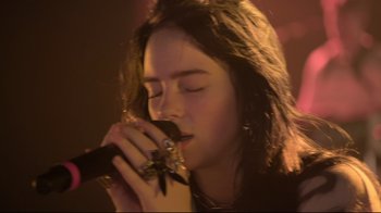 Movie still from “Billie Eilish: The World's a Little Blurry” (2021), directed by R.J. Cutler – A woman is holding a microphone up to her mouth; Close Up shot, Low angle