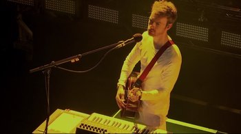 Movie still from “Billie Eilish: The World's a Little Blurry” (2021), directed by R.J. Cutler – A man with a guitar and a keyboard on a stage; Medium shot, High angle