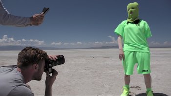 Movie still from “Billie Eilish: The World's a Little Blurry” (2021), directed by R.J. Cutler – A man in a green mask is taking a picture of another man; Medium shot, Low angle