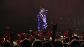 Movie still from “Billie Eilish: The World's a Little Blurry” (2021), directed by R.J. Cutler – A person on a stage singing into a microphone; Wide shot, Low angle