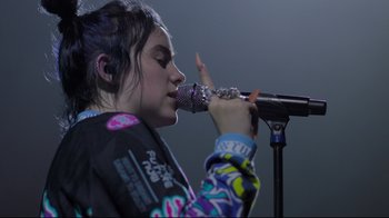 Movie still from “Billie Eilish: The World's a Little Blurry” (2021), directed by R.J. Cutler – A woman with a microphone in her mouth; Close Up shot, High angle