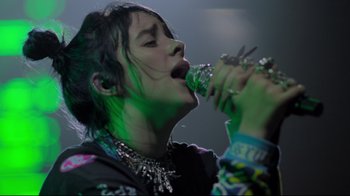 Movie still from “Billie Eilish: The World's a Little Blurry” (2021), directed by R.J. Cutler – A woman is singing into a microphone; Close Up shot, Low angle