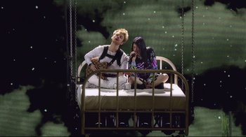 Movie still from “Billie Eilish: The World's a Little Blurry” (2021), directed by R.J. Cutler – A couple of people sitting on top of a bed next to each other; Wide shot, Low angle