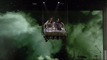 Movie still from “Billie Eilish: The World's a Little Blurry” (2021), directed by R.J. Cutler – Two people are sitting in a bed suspended in the air; Wide shot, Low angle