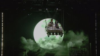 Movie still from “Billie Eilish: The World's a Little Blurry” (2021), directed by R.J. Cutler – A man and a woman are sitting in a bed suspended in the air; Extreme Wide shot, Low angle