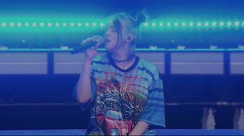 Movie still from “Billie Eilish: The World's a Little Blurry” (2021), directed by R.J. Cutler – A person that is holding a microphone up to their mouth; Medium shot, Low angle