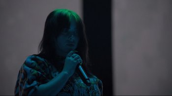 Movie still from “Billie Eilish: The World's a Little Blurry” (2021), directed by R.J. Cutler – A woman holding a microphone in a dark room; Close Up shot, Low angle