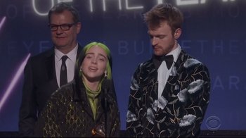 Movie still from “Billie Eilish: The World's a Little Blurry” (2021), directed by R.J. Cutler – A group of people standing next to each other on a stage; Medium shot, Low angle