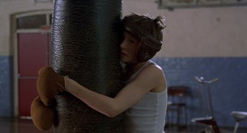 Movie still from “Billy Elliot” (2000), directed by Stephen Daldry – A woman in a boxing helmet is hugging a punching bag; Close Up shot, Low angle