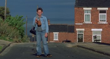 Movie still from “Billy Elliot” (2000), directed by Stephen Daldry – A man standing on the side of the road holding a bag; Wide shot, Low angle
