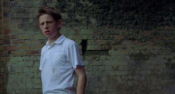 Movie still from “Billy Elliot” (2000), directed by Stephen Daldry – A young boy standing in front of a brick wall; Medium shot, Low angle