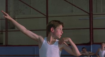 Movie still from “Billy Elliot” (2000), directed by Stephen Daldry – A young man in a white tank top is holding his arms up; Medium shot, Low angle