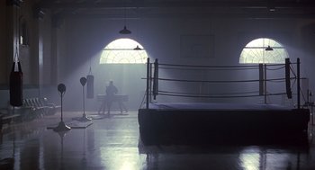 Movie still from “Billy Elliot” (2000), directed by Stephen Daldry – A boxing ring in a room with a person sitting on the bench; Extreme Wide shot, Low angle