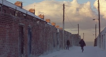 Movie still from “Billy Elliot” (2000), directed by Stephen Daldry – Two people walking down a snowy street near a brick wall; Extreme Wide shot, High angle