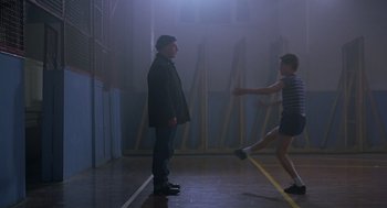 Movie still from “Billy Elliot” (2000), directed by Stephen Daldry – Two people standing in a gym with one of them kicking a ball; Wide shot, Low angle