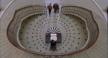 Movie still from “Billy Elliot” (2000), directed by Stephen Daldry – Two people standing in front of a desk in a spiral staircase; Extreme Wide shot, Overhead angle