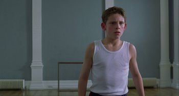Movie still from “Billy Elliot” (2000), directed by Stephen Daldry – A young boy wearing a white tank top standing in front of a blue wall; Medium shot, Low angle