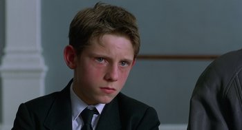 Movie still from “Billy Elliot” (2000), directed by Stephen Daldry – A young man in a suit and tie looking at the camera; Close Up shot, Over the shoulder angle