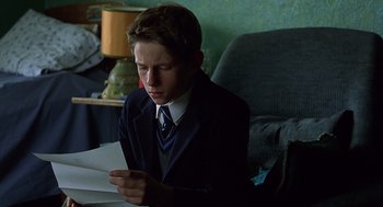 Movie still from “Billy Elliot” (2000), directed by Stephen Daldry – A boy in a suit and tie looking at a piece of paper; Medium shot, Over the shoulder angle