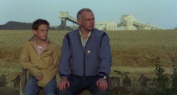 Movie still from “Billy Elliot” (2000), directed by Stephen Daldry – A man sitting next to a boy in a field; Medium shot, Low angle