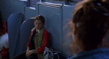 Movie still from “Billy Elliot” (2000), directed by Stephen Daldry – A young boy sitting on a bench with a bag of luggage; Medium shot, Over the shoulder angle