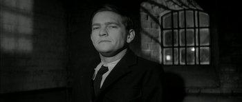 Movie still from “Billy Liar” (1963), directed by John Schlesinger – A black and white photo of a man in a suit and tie; Close Up shot, Low angle