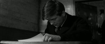 Movie still from “Billy Liar” (1963), directed by John Schlesinger – A man in a suit writing on a piece of paper; Close Up shot, High angle