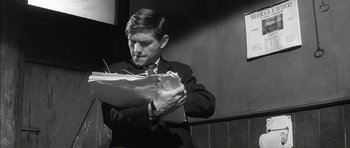 Movie still from “Billy Liar” (1963), directed by John Schlesinger – A man in a suit and tie looking at papers in his hands; Close Up shot, Low angle