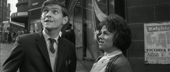 Movie still from “Billy Liar” (1963), directed by John Schlesinger – A man and a woman standing next to each other in front of a building; Medium shot, Low angle