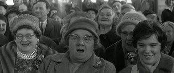 Movie still from “Billy Liar” (1963), directed by John Schlesinger – An older woman with glasses and a hat in a crowd of older people; Medium shot, Low angle
