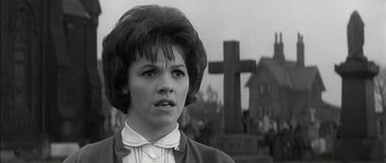 Movie still from “Billy Liar” (1963), directed by John Schlesinger – A woman standing in front of a cross in a cemetery; Close Up shot, Low angle
