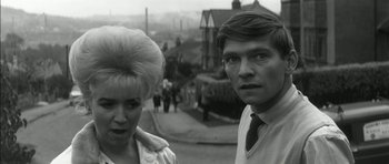 Movie still from “Billy Liar” (1963), directed by John Schlesinger – A man and a woman standing next to each other on a street; Close Up shot, High angle