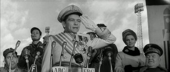 Movie still from “Billy Liar” (1963), directed by John Schlesinger – An old photo of a man saluting in front of microphones; Medium shot, Low angle