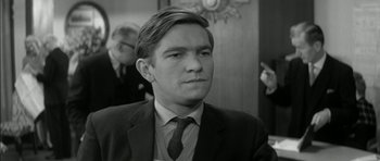 Movie still from “Billy Liar” (1963), directed by John Schlesinger – Black and white photograph of a man wearing a suit and tie; Close Up shot, Over the shoulder angle