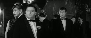 Movie still from “Billy Liar” (1963), directed by John Schlesinger – A black - and - white photo of men in tuxedos; Medium shot, Low angle