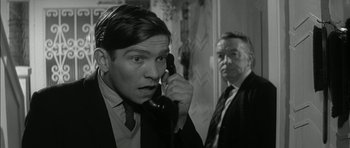 Movie still from “Billy Liar” (1963), directed by John Schlesinger – A man talking on a phone next to another man in a suit; Close Up shot, Over the shoulder angle