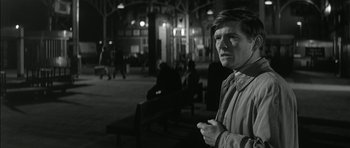 Movie still from “Billy Liar” (1963), directed by John Schlesinger – A man standing on a bench at night in the dark; Medium shot, Over the shoulder angle