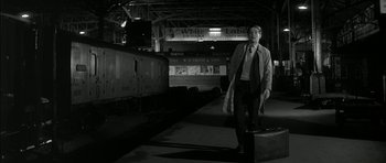Movie still from “Billy Liar” (1963), directed by John Schlesinger – A man standing next to a train on a train platform; Wide shot, Low angle