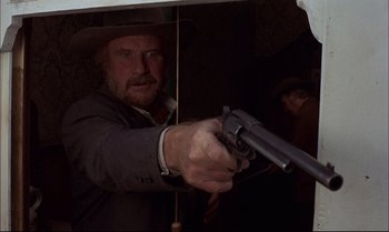 Movie still from “Billy Two Hats” (1974), directed by Ted Kotcheff – A man holding a gun while standing under an umbrella; Close Up shot, Low angle