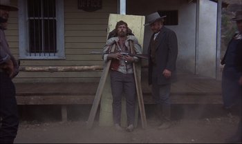Movie still from “Billy Two Hats” (1974), directed by Ted Kotcheff – A man standing next to another man holding a gun; Wide shot, Low angle